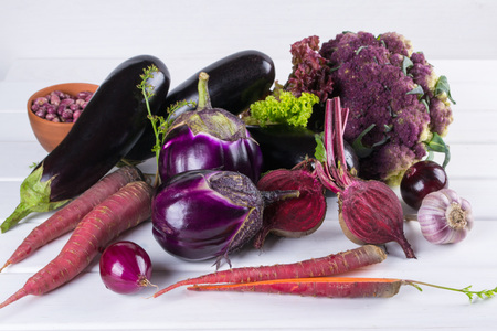 Assortment of fresh raw purple homegrown vegetables on dark wooden table. Cauliflower, eggplant, beets, carrots, potatoes, plums, basil, onions, garlic, beans, lettuce. の写真素材