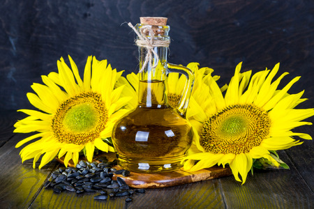 Bright sunflowers with seeds and bottle of oil on wooden table close upの写真素材