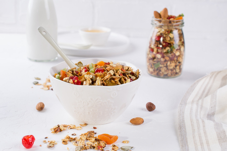 Healthy breakfast concept. Baked granola in white ceramic bowl and glass jar on the kitchen table.の写真素材