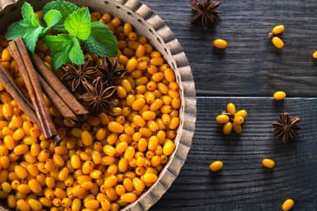 Fresh ripe organic sea buckthorn berries in wooden bowl with cinnamon sticks, anise stars and mint...
