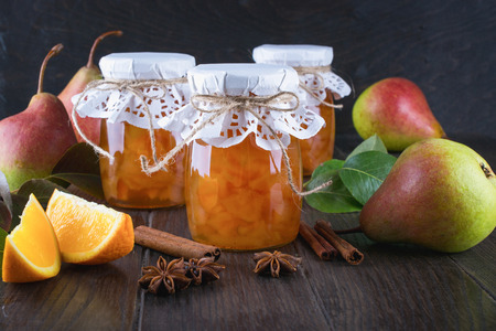 Pear and orange jam in  glass jars with ripe pears, cinnamon sticks, anise stars and green  leaves on the table.の写真素材