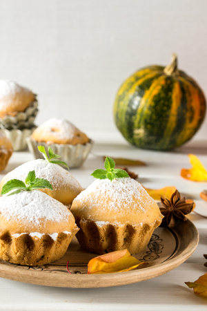 Autumn pastries. Homemade cupcakes with powdered sugar with cinnamon sticks, anise stars, pumpkins, berries of rose hip and autumn leavesの写真素材