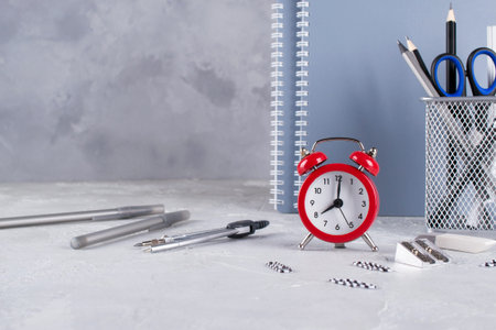 Back to school. Items for the school, red alarm clock on a gray concrete table