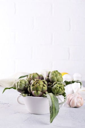 Fresh artichoke preparing for cooking with garlic, lemon and olive oil, kitchen interior.の写真素材