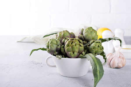 Fresh artichoke preparing for cooking with garlic, lemon and olive oil, kitchen interior.の写真素材