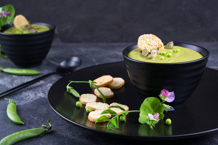 Green pea soup puree with croutons in black bowl.  On dark stone backgroundの写真素材