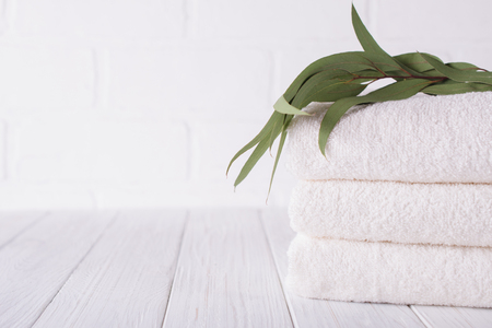 Spa composition on wooden table. Stack of three white fluffy bath towels with eucalyptus branch. Copy spaceの写真素材