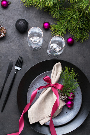Christmas or New Year table setting with christmas pine branches, holiday decorations knife, fork ,ribbon and plate. Menu concept on dark backgroundの写真素材