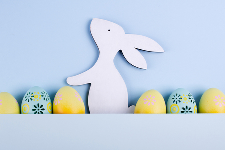 Easter holiday background with eggs. Top view of colorful painted chicken eggs plased  in a row and decorative wooden bunnyの写真素材