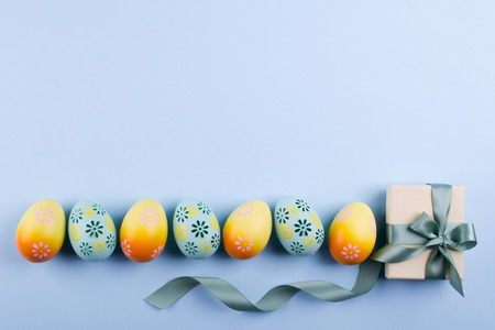 Easter holiday background with eggs. Top view of colorful painted chicken eggs plased  in a row and present box with ribbonの写真素材