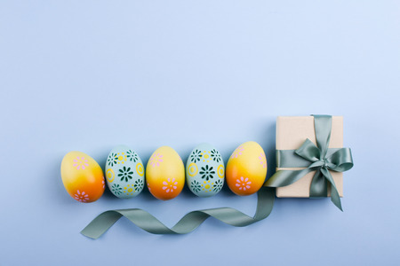 Easter holiday background with eggs. Top view of colorful painted chicken eggs plased  in a row and present box with ribbonの写真素材