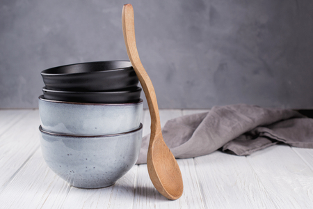 Stack of rustic style handcraft bowls in neutral tones against shabby grey wall with wooden spoon.の写真素材