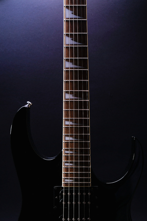 Body and neck of electric guitar. Close up detail. Accentuated shapes by illumination. With copy space on dark backgrounaの写真素材