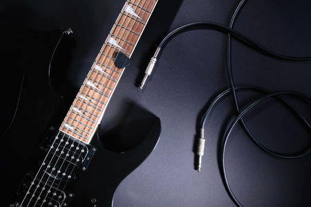 Modern black electric guitar with jack cable on black backgroundの写真素材