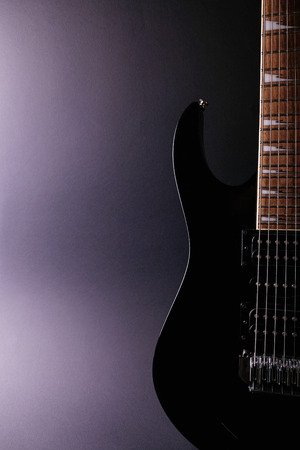 Body and neck of electric guitar. Close up detail. Accentuated shapes by illumination. With copy space on dark backgrounaの写真素材
