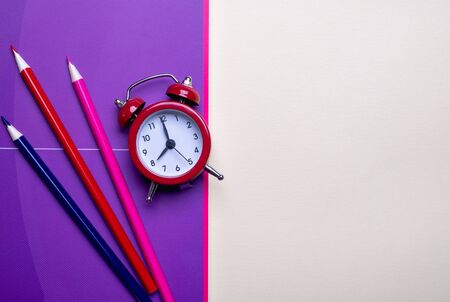 Time management concept. Red vintage alarm clock, pencils and purple  notepadの写真素材
