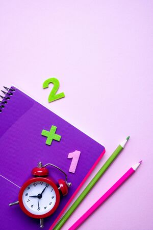 Colorful pencils lying on a purple notebook and red alarm clock. Back to school concept. Time management. Top viewの写真素材