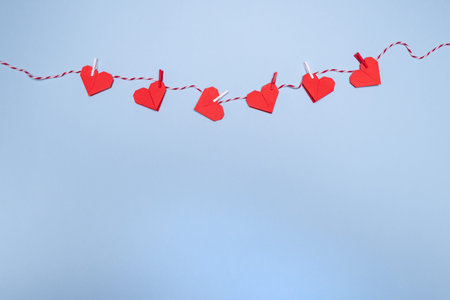 Red origami hearts on rope with clothespins, on a pastel blue background. Place for text, copy...