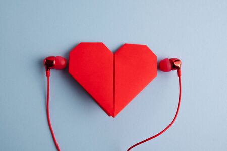 Listen to your heart. Red origami heart with headphones on blue background. Love listening to musicの写真素材