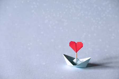 Valentine's day greeting card. Origami boat with heart flag on glitter blue background Romantic, Valentines day concept with space for text.の写真素材