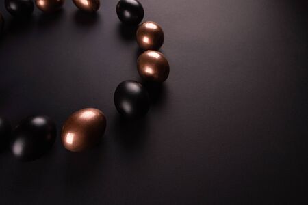 Golden and black eggs, laid out in a circle on black background. Flat lay, Top view, copy space.の写真素材