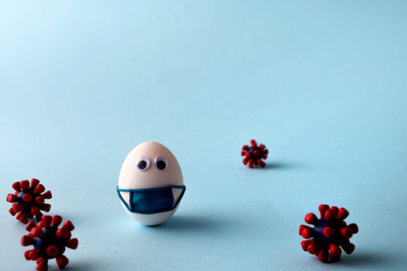 Eggs wearing medical mask for stop coronavirus and models of covid-19 virus on blue background....
