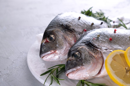 Fresh raw sea bream fish decorated with lemon slices, herbs on gray background. Healthy food...