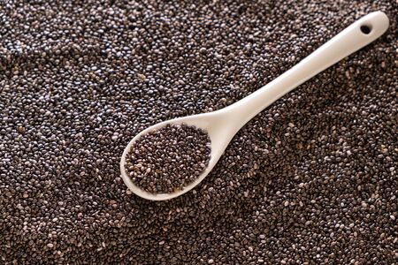 Chia seeds in a white ceramic spoon on a pile of seeds top view.の写真素材