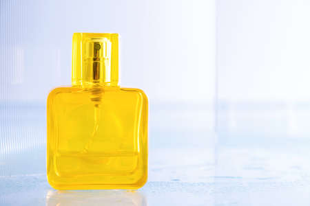 Empty yellow bottle of perfume over blue ceramic tile background with drops of waterの写真素材