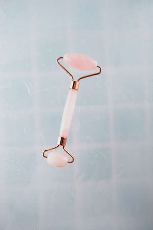 Pink face roller massager made from natural quartz stone over blue ceramic tile background with drops of water Lifting and toning treatment at home.の写真素材