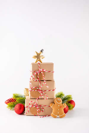 Stack of Christmas gifts boxes in craft paper with crunchy gingerbread men cookies and bright decoration. Merry Christmas concept on white backgroundの写真素材