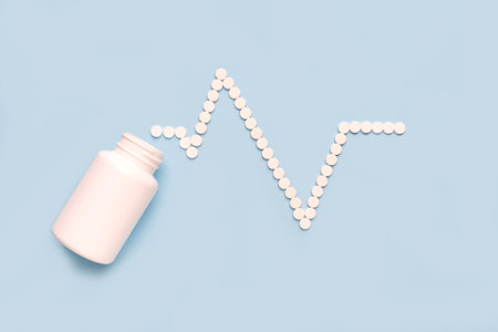 Pills in shape of cardiogram and heart pulse spilled from a white bottle. Pharmaceutical and cardiology concepts.の写真素材