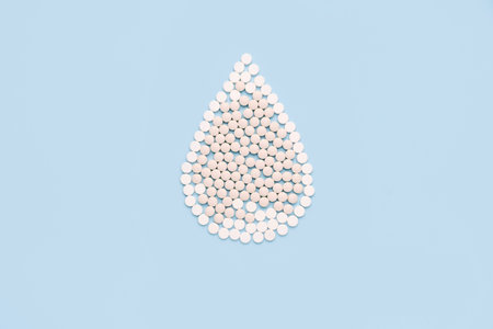 Drop of blood made pills on blue background. Concept of give blood donation, blood transfusion. World hemophilia day.の写真素材
