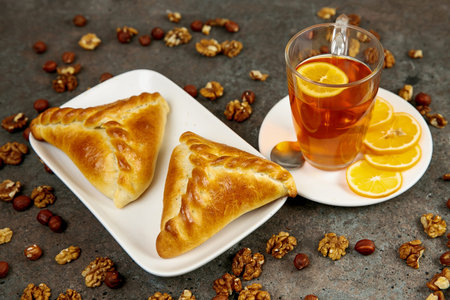 Triangular pies with meat on a white square plate. Transparent cup with lemon tea