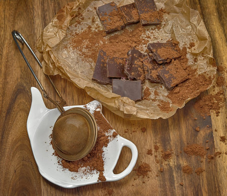 Dark chocolate pieces on craft paper and strainer with cocoa.の写真素材