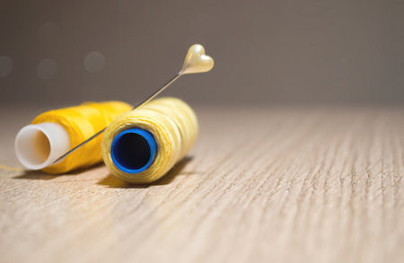 Two yellow spools of thread and a pin on the table on a blurry backgroundの写真素材