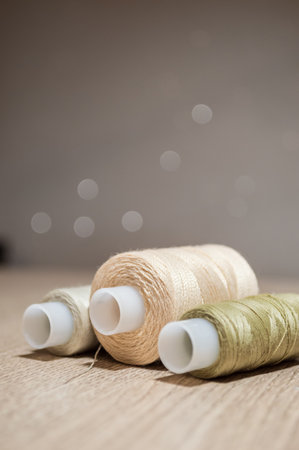 Three spools of beige thread on the table on a blurry backgroundの写真素材