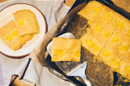Yellow orange homemade pie, cut into pieces, on a baking sheet, plate with a piece of fruitcake