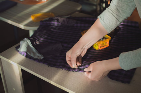 Dressmaker's hands sewing purple skirt with needle and thread on table in sunlight