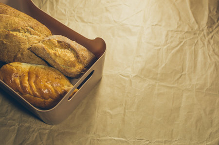 Freshly baked homemade rye wheat bread with golden crust in plastic basket on crumpled craft paper, copy spaceの写真素材