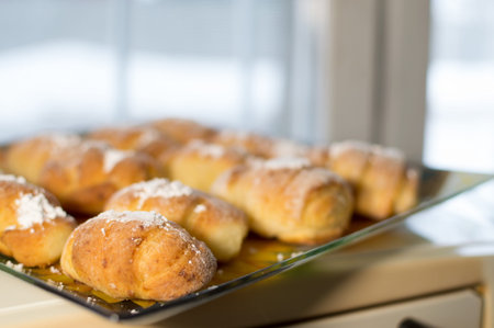 Ruddy homemade pastries, oblong rolls with stuffing, stacked in rows on plate and sprinkled with powdered sugarの写真素材
