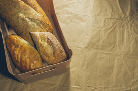 Freshly baked homemade rye wheat bread with golden crust in plastic basket on crumpled craft paper, copy spaceの写真素材