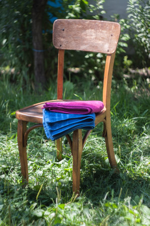 Pile of  bright blue and red crimson towels on old vintage retro chair on green grass in sunlight and shadows, concept of washing in bathの写真素材