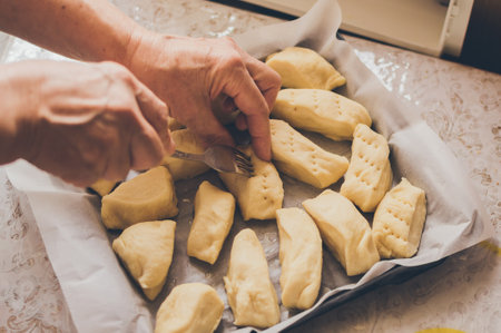 Women's hands making sweet dough buns, laying cakes in rows on a baking sheetの写真素材