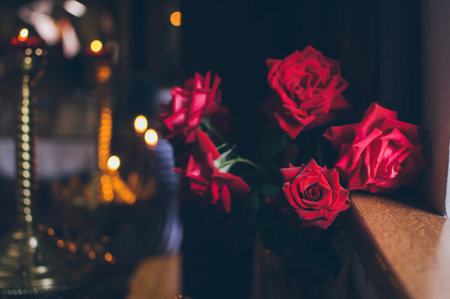 A bouquet of dark red velvet roses by the window in the dark, the semi-darkness of the church with candlesticksの写真素材