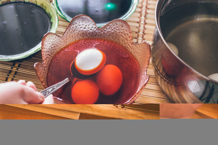 Coloring eggs for Easter in red paint. Lowering egg with spoon into colored liquid in plateの写真素材