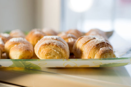 Ruddy homemade pastries, oblong rolls with stuffing, stacked in rows on plate and sprinkled with powdered sugarの写真素材