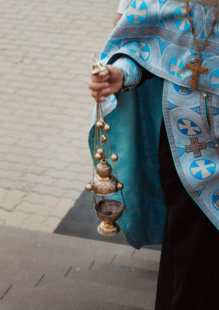 Orthodox priest in blue vestments prayerfully waves a censer in the church