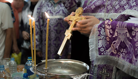 The hands of a priest with a large gilded Christian cross consecrate water in a vessel in the Orthodox Churchの写真素材