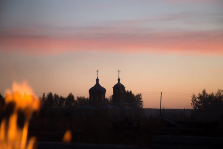 Silhouette of church houses with crosses against a crimson red-orange blue evening sky, flames of...